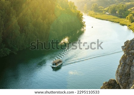 river bus transports people along the river on a summer evening aerial view, forest and cliff edge. the rays of the sun at sunset