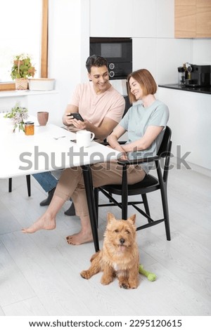 Young married couple sitting in the kitchen and taking a selfie with smartphone while their cute pet feeling sad because of the lack of attention