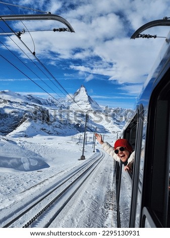 A happy girl taking a picture in a train with the beautiful matterhorn mountain in the background.