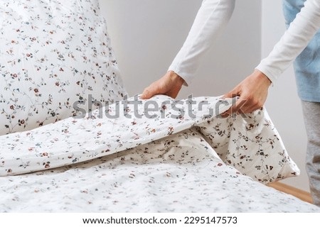 Concept of hotel service, household and chores. Close up view of woman makes bed in her bedroom. Spring cleaning and change of linen. Female hold blanket with a clean duvet cover in a flower pattern Royalty-Free Stock Photo #2295147573