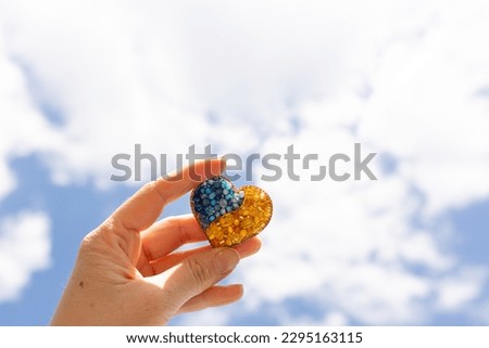 brooch in the shape of a heart in yellow-blue color against the sky. colors of the flag of Ukraine, yellow-blue heart