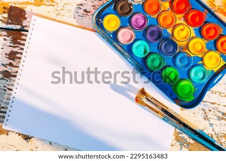 Set of watercolor paints, paint brushes and paper on wooden background.