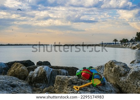 Sunrise in a beautiful sea bay in Italy, children's toys on a stone embankment, seagulls in the sky over the sea, authentic sustainable development in unity with nature, horizon