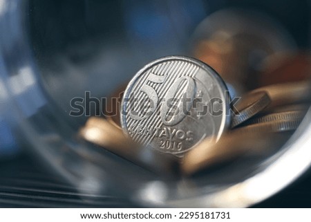 Brazilian coins inside a glass jar. Highlight for 50 cents coin. Brazilian economy. Dark environment. Macro photography. Royalty-Free Stock Photo #2295181731