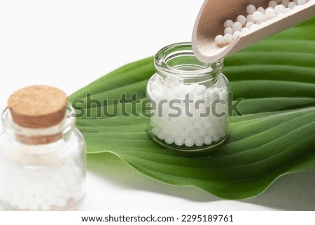 Pouring homeopathic granules from a wooden scoop into a bottle Royalty-Free Stock Photo #2295189761