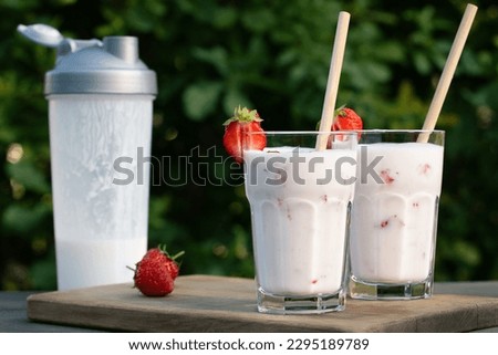 Protein shake from yogurt and strawberries in a shaker and two glass glasses on a wooden table