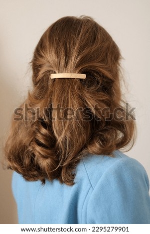 Young woman with thick, natural blonde hair pulled back and pinned half-up by a barrette hair clip. Gold metal barrette. Pretty hairstyle. Elegant hairstyle. Blue coat.  Royalty-Free Stock Photo #2295279901