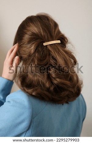 Young woman with thick, natural blonde hair pulled back and pinned half-up by a barrette hair clip. Gold metal barrette. Pretty hairstyle. Elegant hairstyle. Blue coat.  Royalty-Free Stock Photo #2295279903