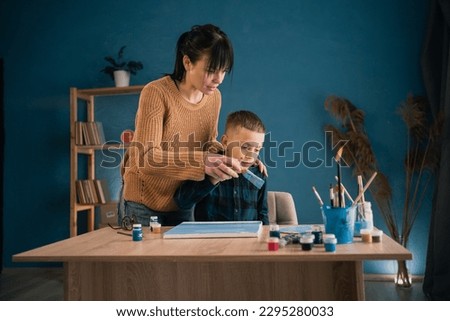 happy young mother helps son to paint acrylic painting on canvas at home. concept of joint pastime. copy space.