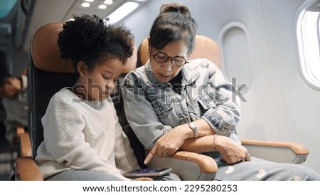 Mother and daughter sitting in passenger airplane using smartphone enjoy watching cartoon waitting for airplane landing