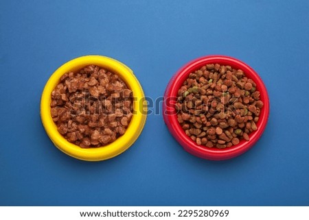 Wet and dry pet food in feeding bowls on blue background. Top view Royalty-Free Stock Photo #2295280969