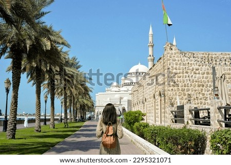 A woman in a long dress with a backpack walks along the Al Majaz embankment, Lake Khaled, Sharjah emirate. Rear view of a woman walking in the park