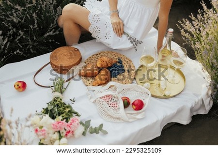 Cropped picture of a girl sitting on picnic. Concept of having picnic in a lavender field during summer holidays or weekends. Girl in a summer dress.