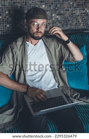 Young bearded man works on a laptop, uses a smartphone, a freelancer, a computer, financial analyst, a sales manager, prepares a report, charts, crypto-currencies in cafe, hipster, beard brutal. 