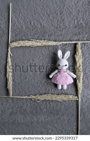 A rabbit in a pink dress sits on a gray rug.
