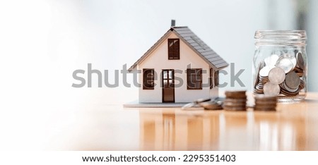 Real estate concept background. House model and coins stack on wooden table, copy space. Royalty-Free Stock Photo #2295351403