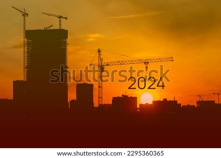 The tower crane set the numbers 2024, the symbol of the new year 2024, the black silhouette of the building on the background, the construction site on the dome of the sun. orange sun contrary light