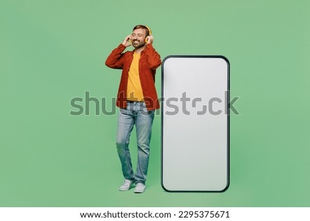 Full body elderly man 40s years old wears casual clothes red shirt t-shirt headphones big huge blank screen mobile cell phone with area listen to music isolated on plain pastel light green background
