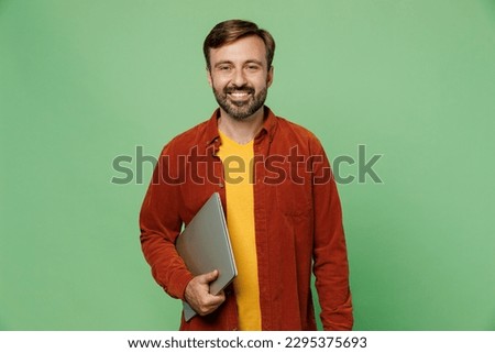 Elderly smiling fun cheerful happy cool IT man 40s years old he wears casual clothes red shirt t-shirt hold closed laptop pc computer isolated on plain pastel light green background studio portrait