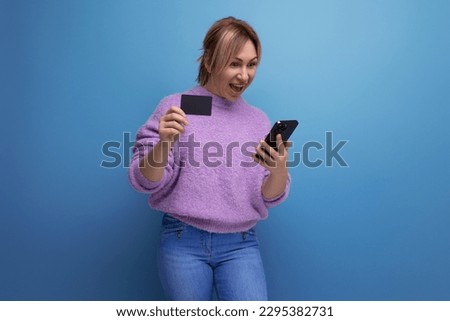 portrait of a beautiful blond young woman in a lilac sweater making an online purchase holding a plastic card with a mockup on a bright background with copy space