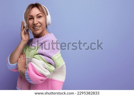 young bright blond girl listens to music in big white headphones on a purple background with copy space