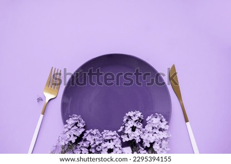 
beautiful layout with lilacs, a plate and cutlery on a purple background. place for text. spring food concept for restaurant or cafe.