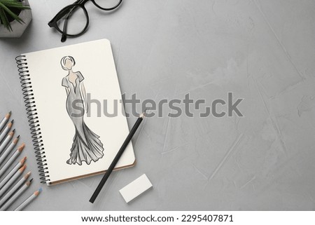 Sketch of beautiful dress in pad on grey textured table, space for text. Fashion designer's desk with stationery, flat lay