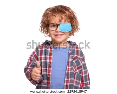 Happy boy with eye patch on glasses showing thumb up against white background. Strabismus treatment