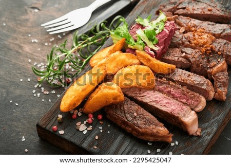 Steaks. Sliced grilled meat steak New York, Ribeye or Chuck roll with with garnished with salad and french fries on black marble board on old wooden background. Top view. Mock up.