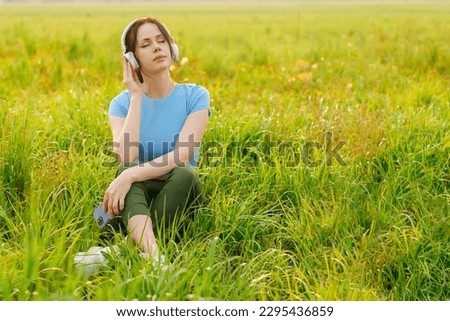 A woman  in listening to music in headphones, closing her eyes as Outside, surrounded by nature,deep relaxation, embracing the tranquility of the moment. Royalty-Free Stock Photo #2295436859