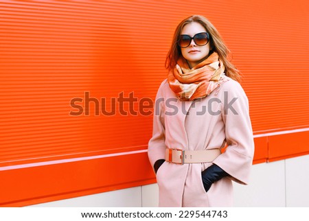 Beauty, fashion, shopping and people concept - pretty stylish woman in coat and sunglasses posing outdoors against colorful wall in the city Royalty-Free Stock Photo #229544743
