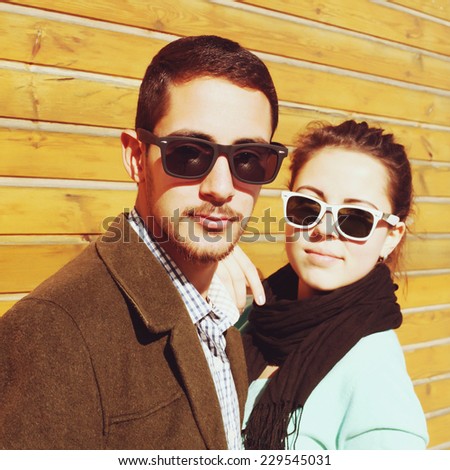 Fashion portrait of happy smiling young vintage hipster pretty couple having fun outdoor on the street. Modern urban people, wooden background. Photo toned style Instagram filters.