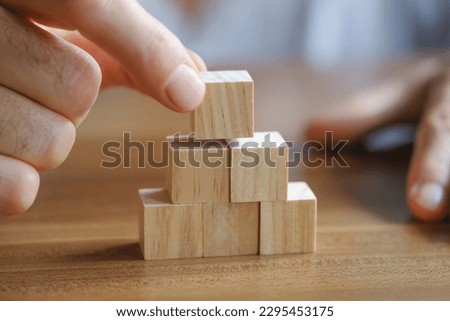 Close-up photo of man putting wooden block on top of pyramid. Planning business growth. Horizontal concept with copy space for your text.