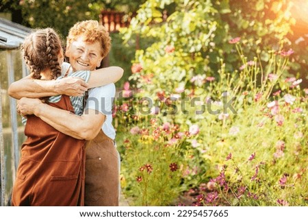 Young teenager girl with cute hairstyle two braids hugging her happy loving grandmother at summer countryhouse outdoor. Copy space text. Royalty-Free Stock Photo #2295457665