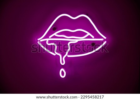 Purple neon sign with leaking saliva from female lips on wall of nightclub. Street wall illuminated by bright neon advertisement