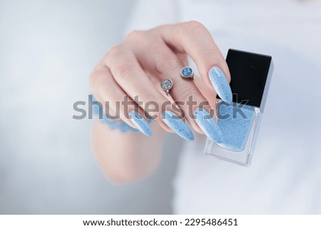 Female hand with long nails and light baby blue manicure with bottles of nail polish