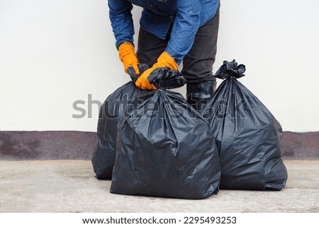 Closeup man holds black plastic bag that contains garbage inside. Concept , Waste management. Environment problems. Daily chores. Throw away rubbish .                               Royalty-Free Stock Photo #2295493253