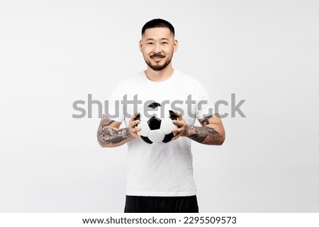 Smiling Asian man holding ball, watching football isolated on white background. Handsome male playing soccer, hobby concept
