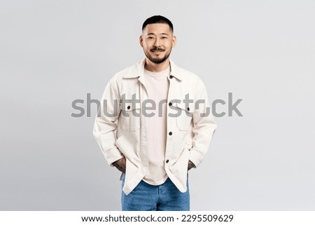 Portrait of successful Asian businessman wearing modern casual clothes isolated on gray background. Attractive male looking at camera hands in pockets