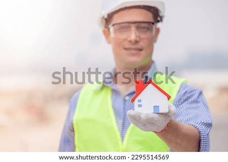 Engineer wears a reflective vest. Glasses and helmets. In his hand held a model of a wooden house Represents home design Or build a house.