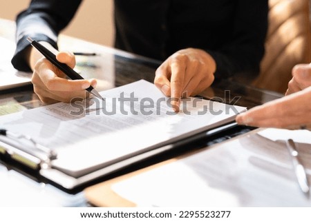 Close-up Of Two Businesspeople Hand Working On Contract Paper Over Desk