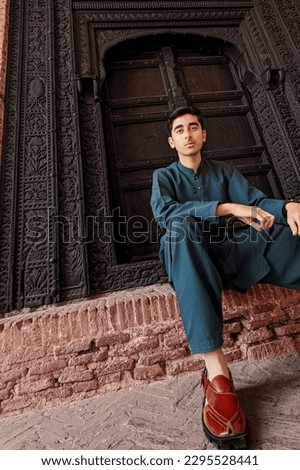Pakistani style photo of a guy wearied Pakistani national clothes shalwar kameez with Peshawari Khari shoes on the front of Asian black door. Dramatic style photo for making banners or posters