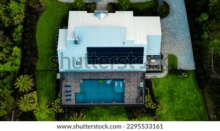Aerial view of a modern home with solar panels and a huge pool, complete with immaculate landscaping