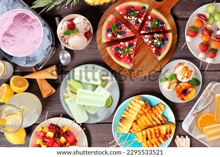 Refreshing summer food table scene. Assorted grilled fruits, ice cream and ice pops. Above view on a dark wood background.