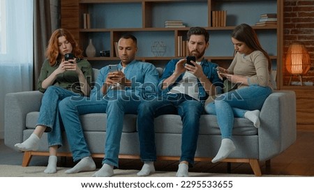 Group friends business people sit on couch with mobile phones chatting in social media ignoring each other multiethnic addicted women and men use diverse devices modern tech addiction gadgets overuse