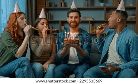 Birthday man happy adult bearded guy hold festive cake burning candles diverse group friends congratulate surprise event celebration at home multiracial men and women blowing whistles festival party