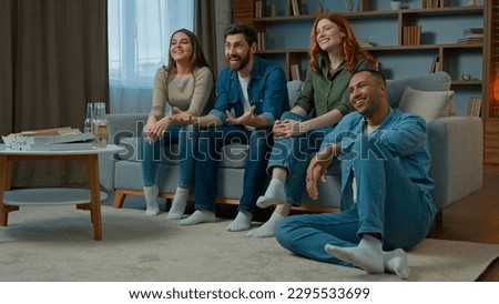 Four diverse ethnicity friends watch television at home cinema people spectators watching smart tv channel comedy show serial movie multiracial african american caucasian women men laughing enjoy film Royalty-Free Stock Photo #2295533699