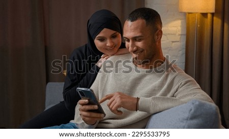 Family couple multiethnic interracial family African American man chatting on mobile phone muslim woman wife cuddle to husband use cellphone shopping online together watch funny internet video at home Royalty-Free Stock Photo #2295533795
