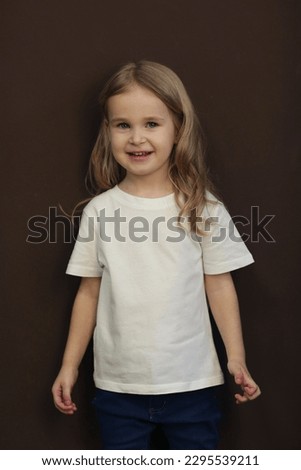 cute blond little girl in white t-shirt and jeans close up photo on dark brown background