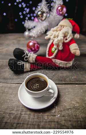 Composition of santa claus with cup of coffee and Christmas decorations on table on bokeh background
